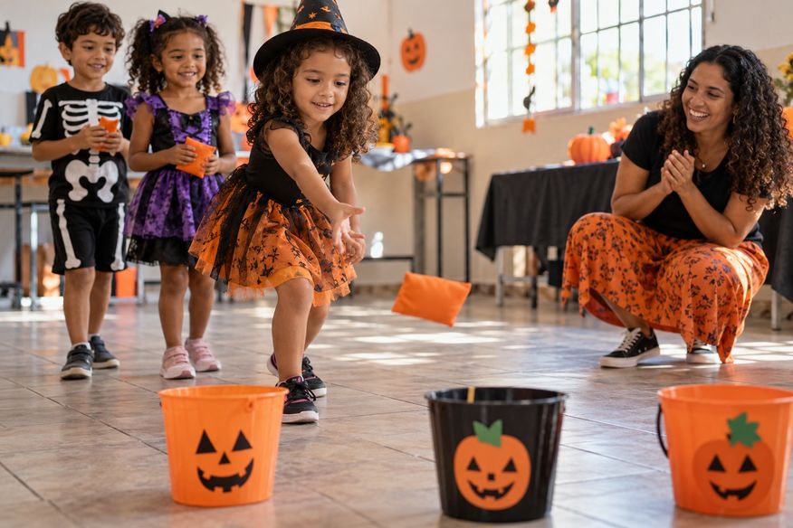 Crianças brincam de arremessar saquinhos em baldes decorados de Halloween