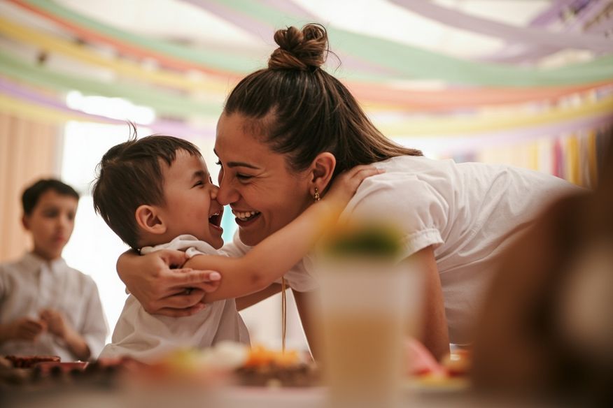 Mãe abraçando o filho pequeno durante festa infantil, com bandeirinhas coloridas penduradas no teto