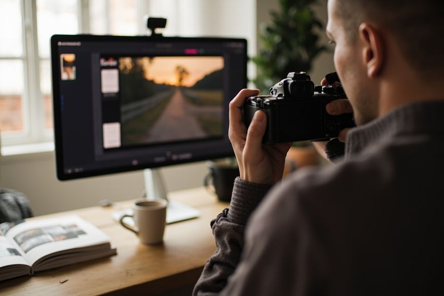 Fotógrafo editando fotos em monitor calibrado, com álbum impresso ao lado, luz suave de janela