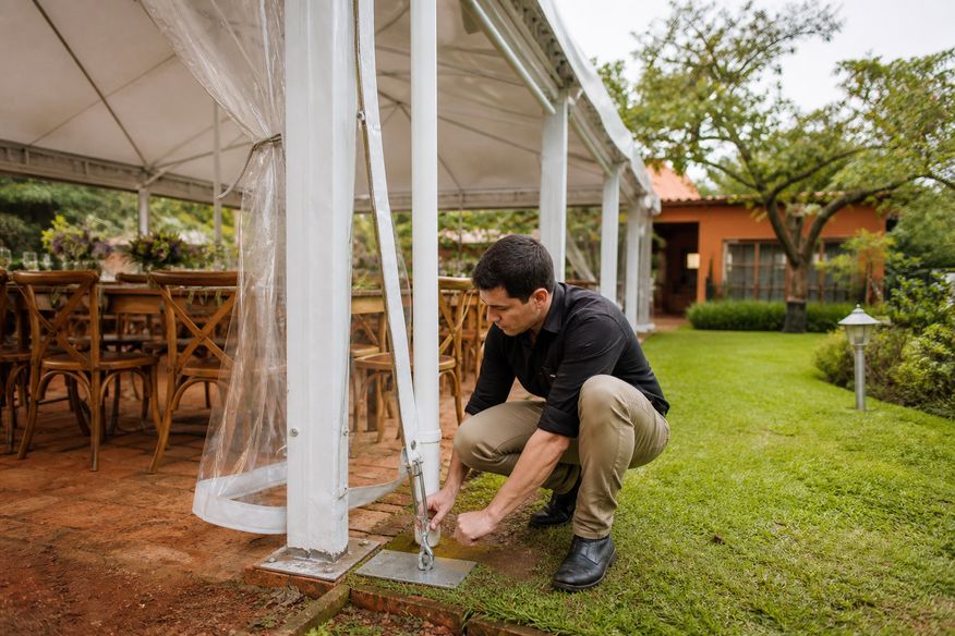 Profissional verifica fixação e drenagem de tenda antes de evento ao ar livre