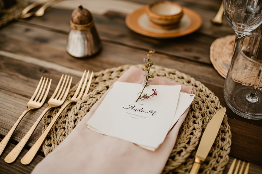 Detalhe de mesa rústica de casamento com sousplat de palha, flores secas e talheres dourados sobre madeira