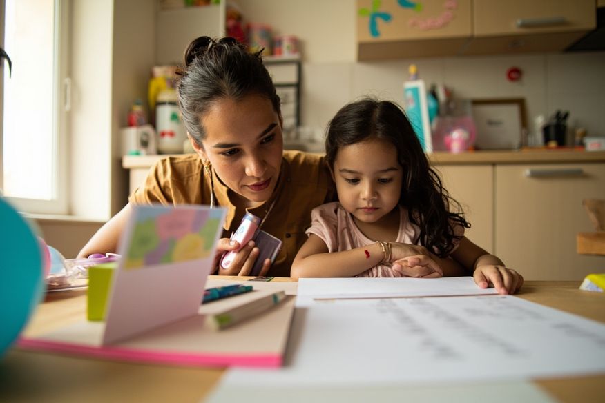 Mãe e filha reviewing orçamento impresso da festa na mesa da cozinha com balões ao redor
