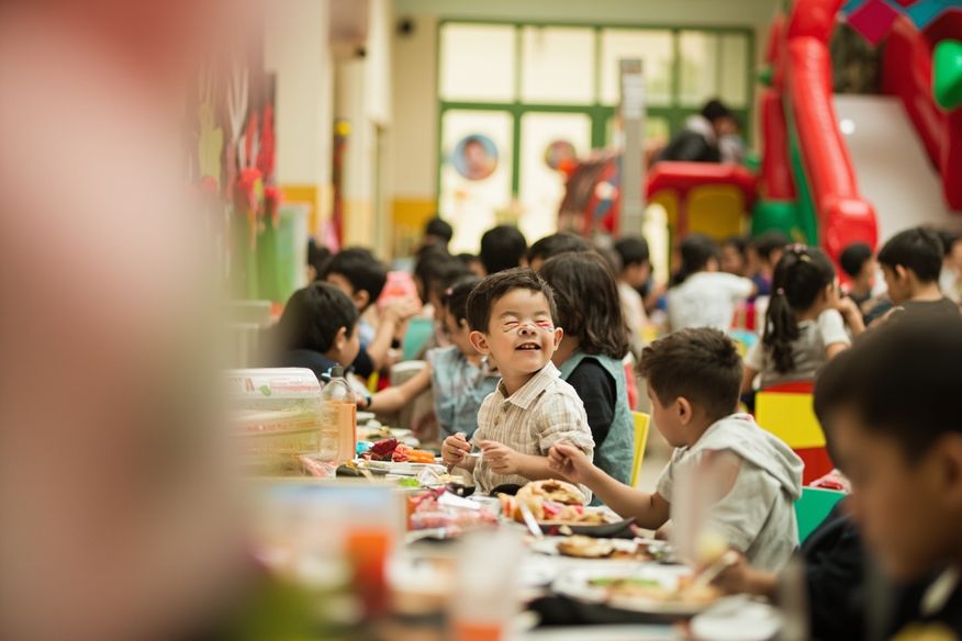 Salão de festa infantil com tobogã inflável, decoração temática e famílias sentadas às mesas